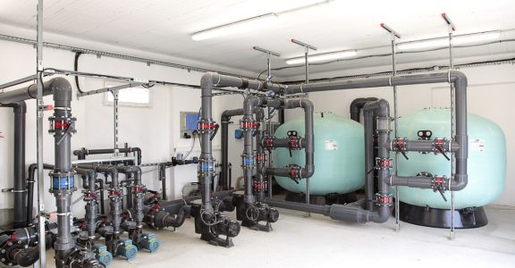 Local technique d’une piscine collective, avec ses filtres et ses canalisations